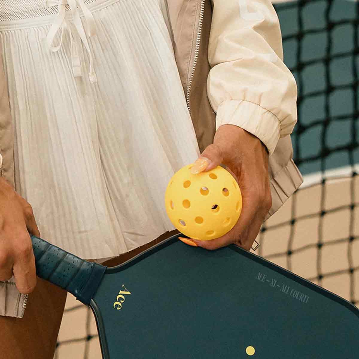 Person holding a pickleball paddle and yellow ball on a court