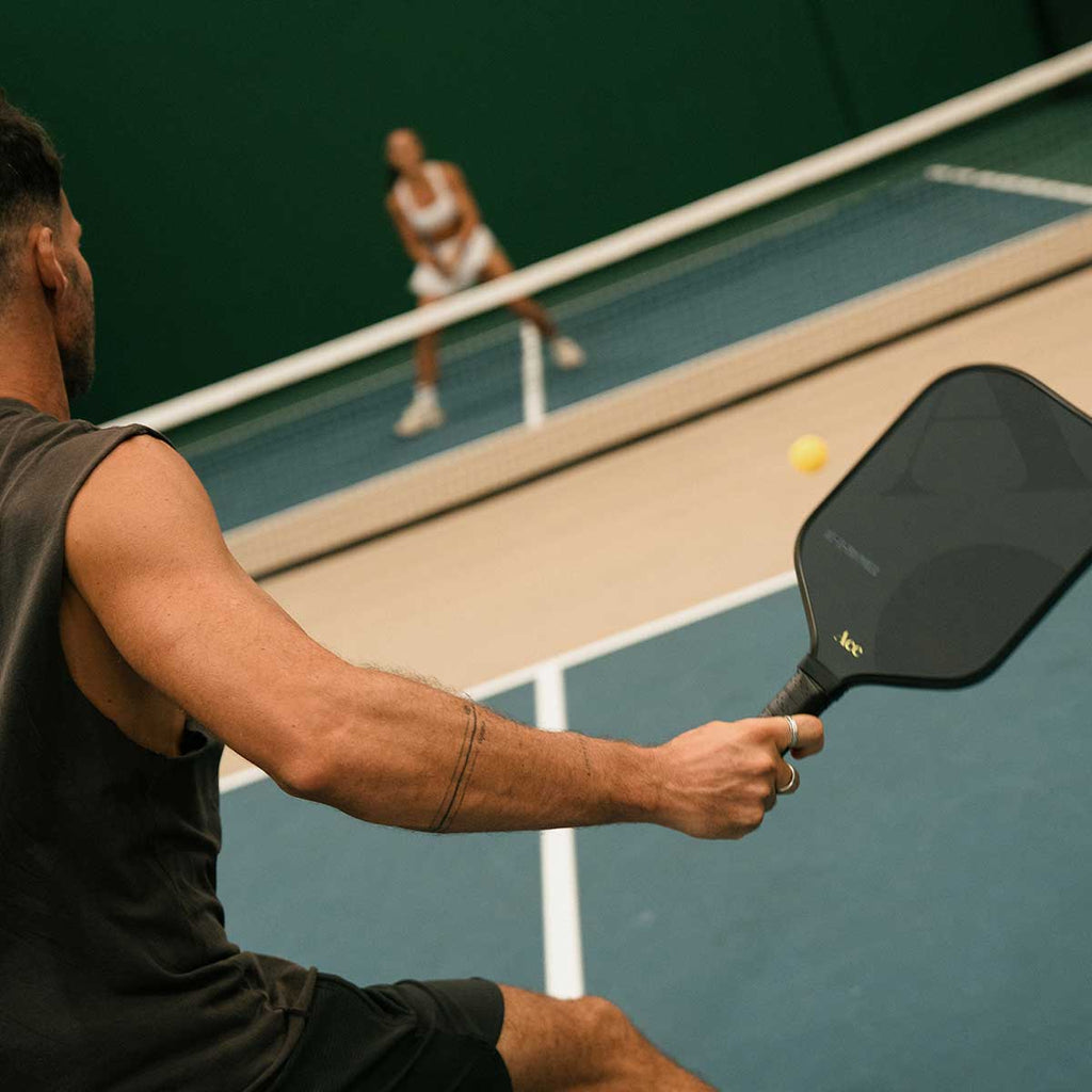 Person playing pickleball on a court with another player in the background.