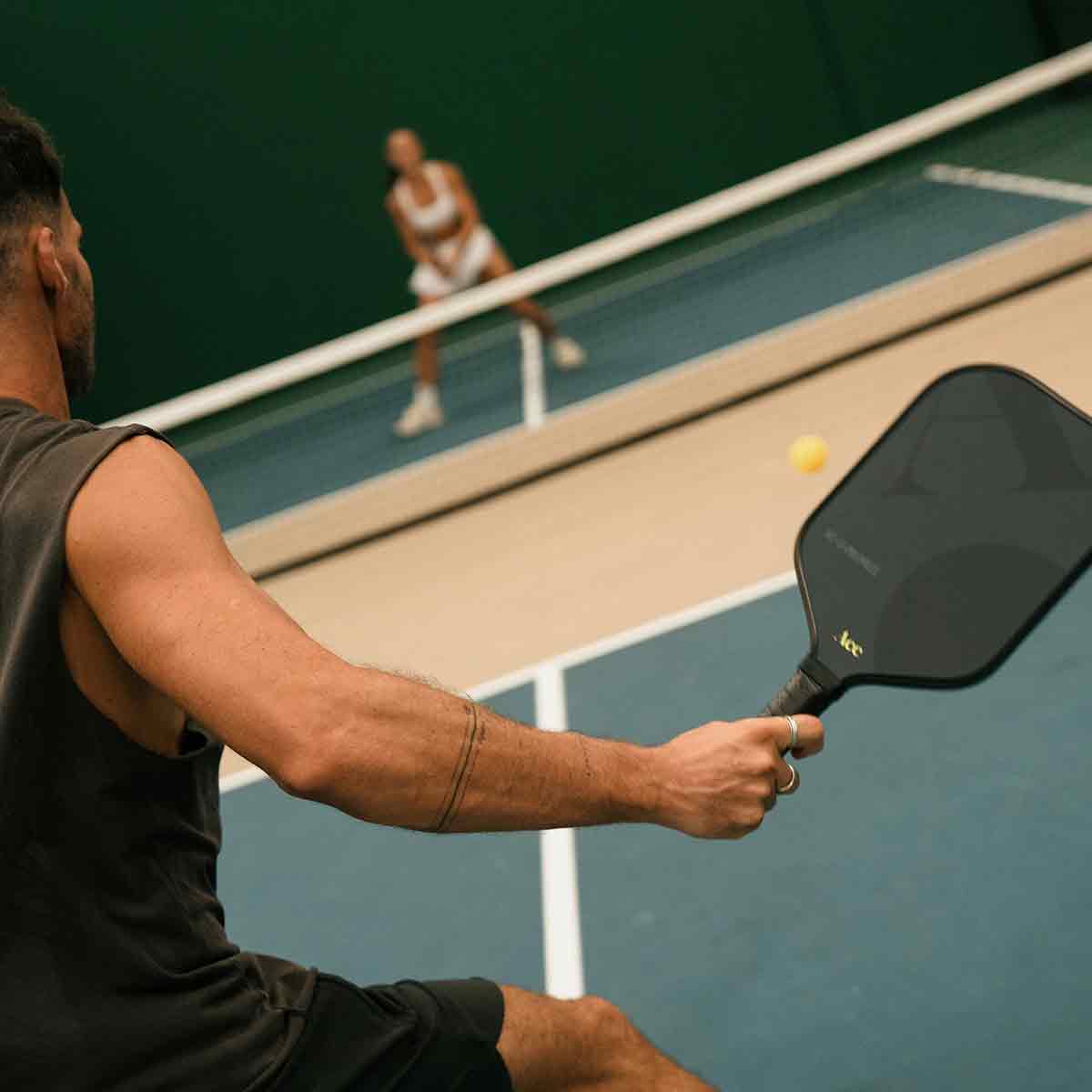 Person playing pickleball on a court with another player in the background.