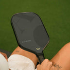 Person holding a pickleball paddle with a green court background