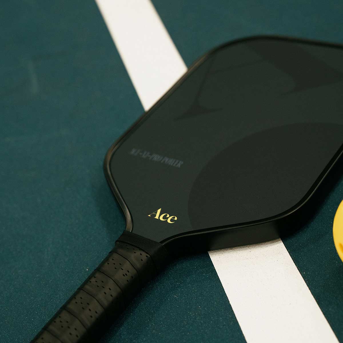Black pickleball paddle with 'Ace' branding on a green court surface