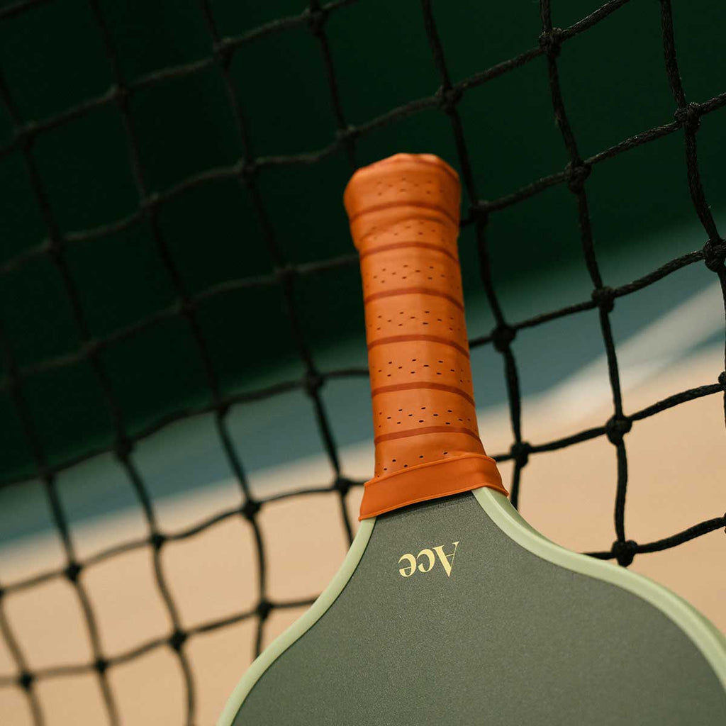 Green pickleball paddle with orange handle against a net background