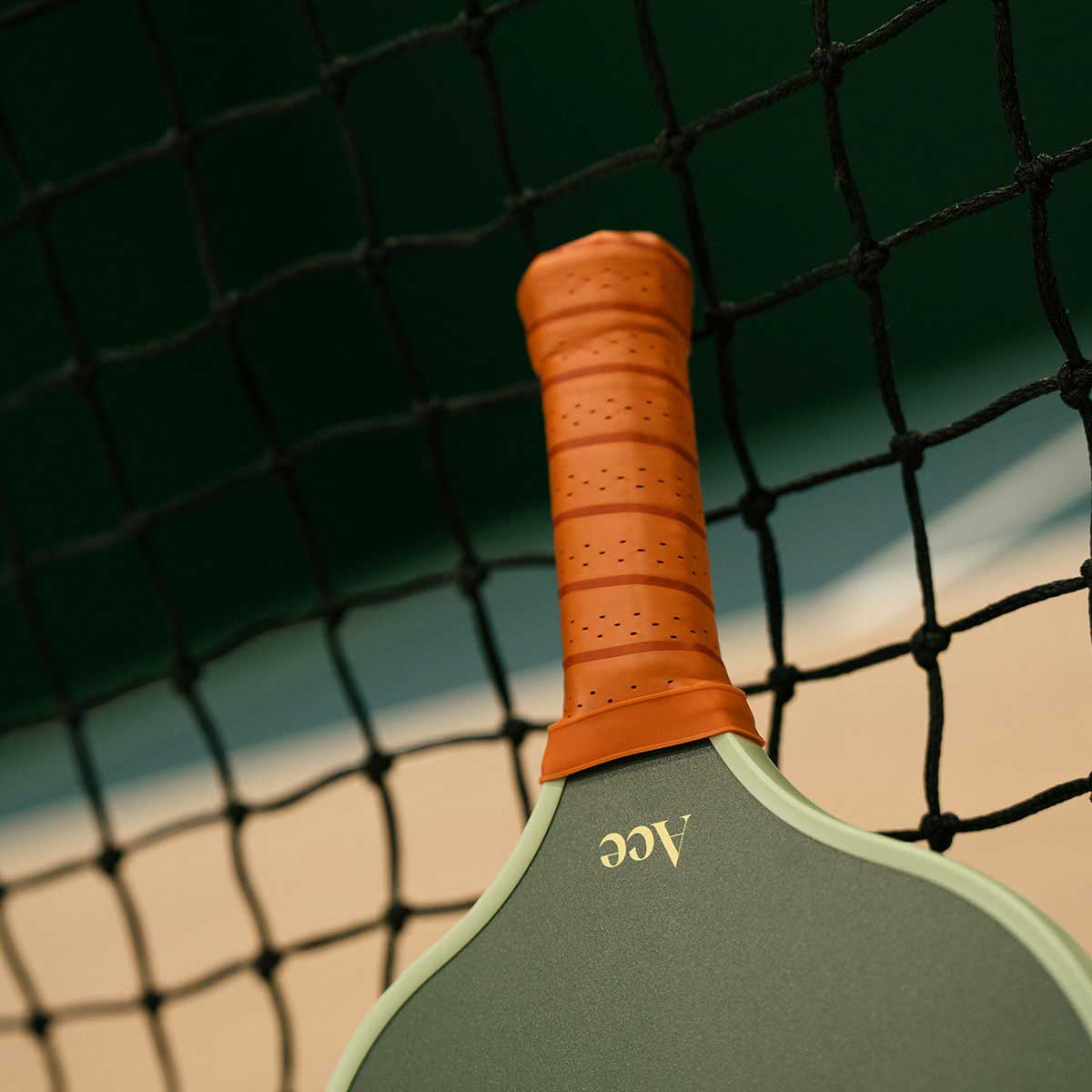 Green pickleball paddle with orange handle against a net background