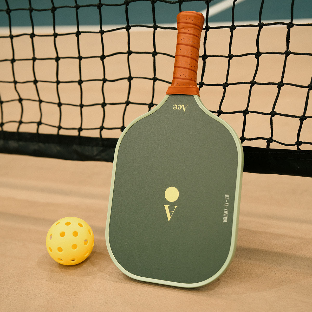 Green pickleball paddle with brown handle on a court with a yellow ball.