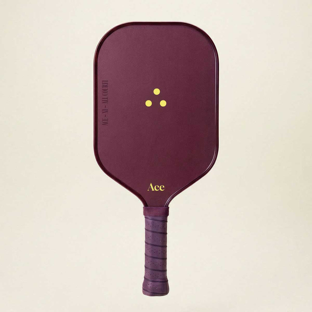 Maroon pickleball paddle with yellow branding on a beige background
