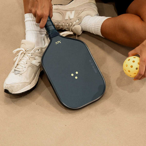 Person holding a pickleball paddle and ball on a beige surface