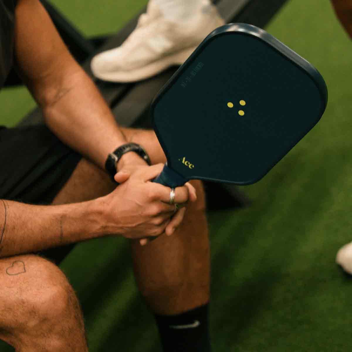 Person holding a pickleball paddle with 'Ace' branding on a green court.