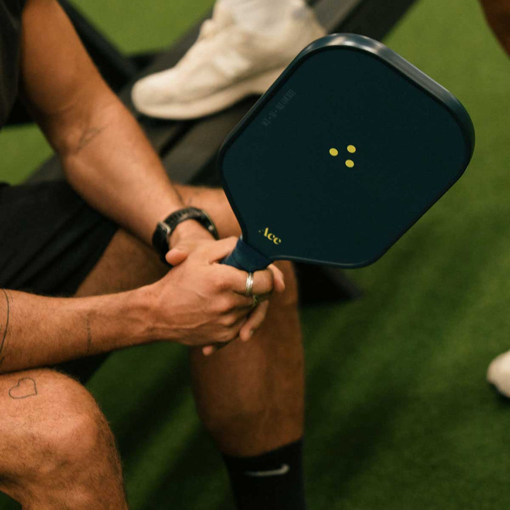 Person holding a pickleball paddle with 'Ace' branding on a green court.
