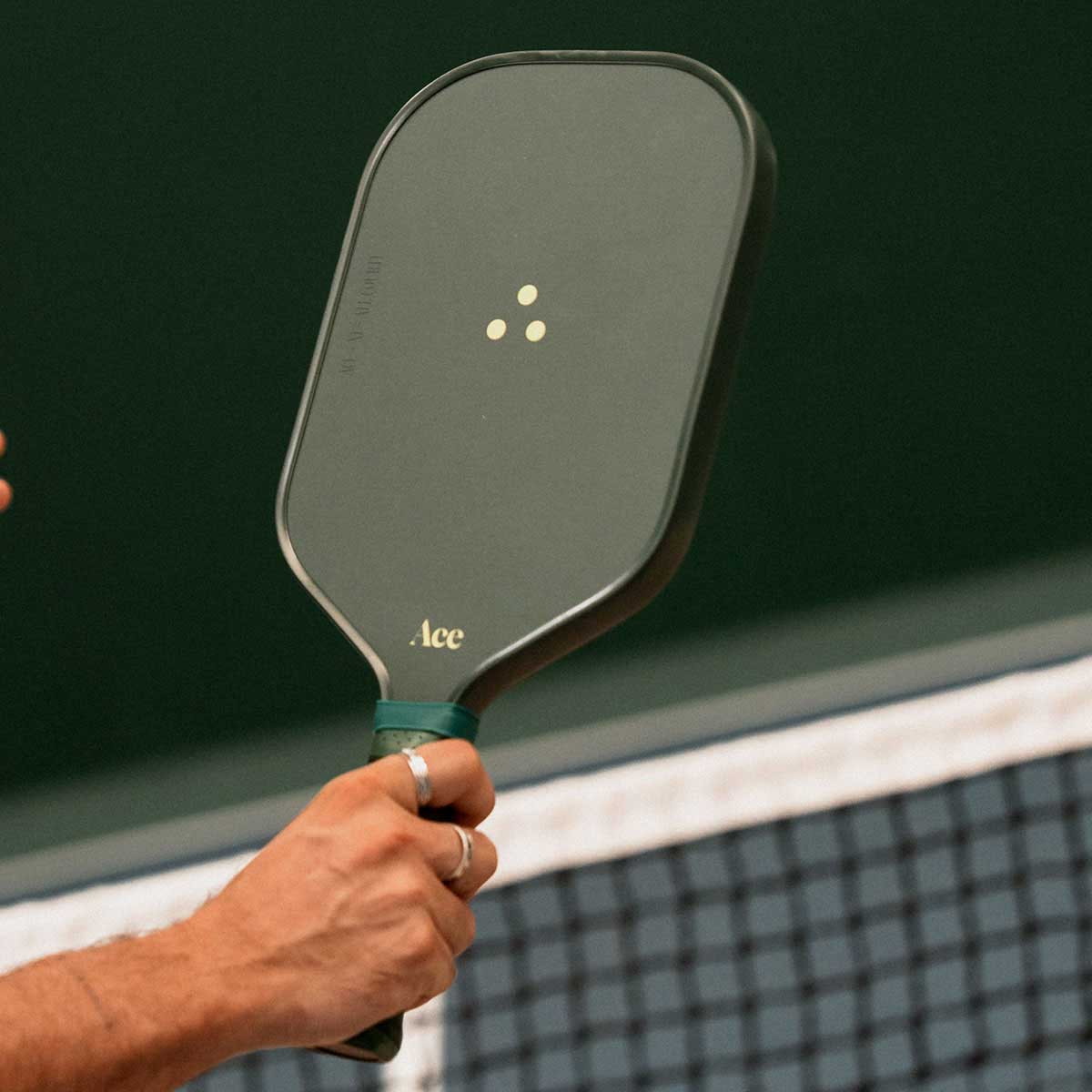 Hand holding a pickleball paddle with a green background