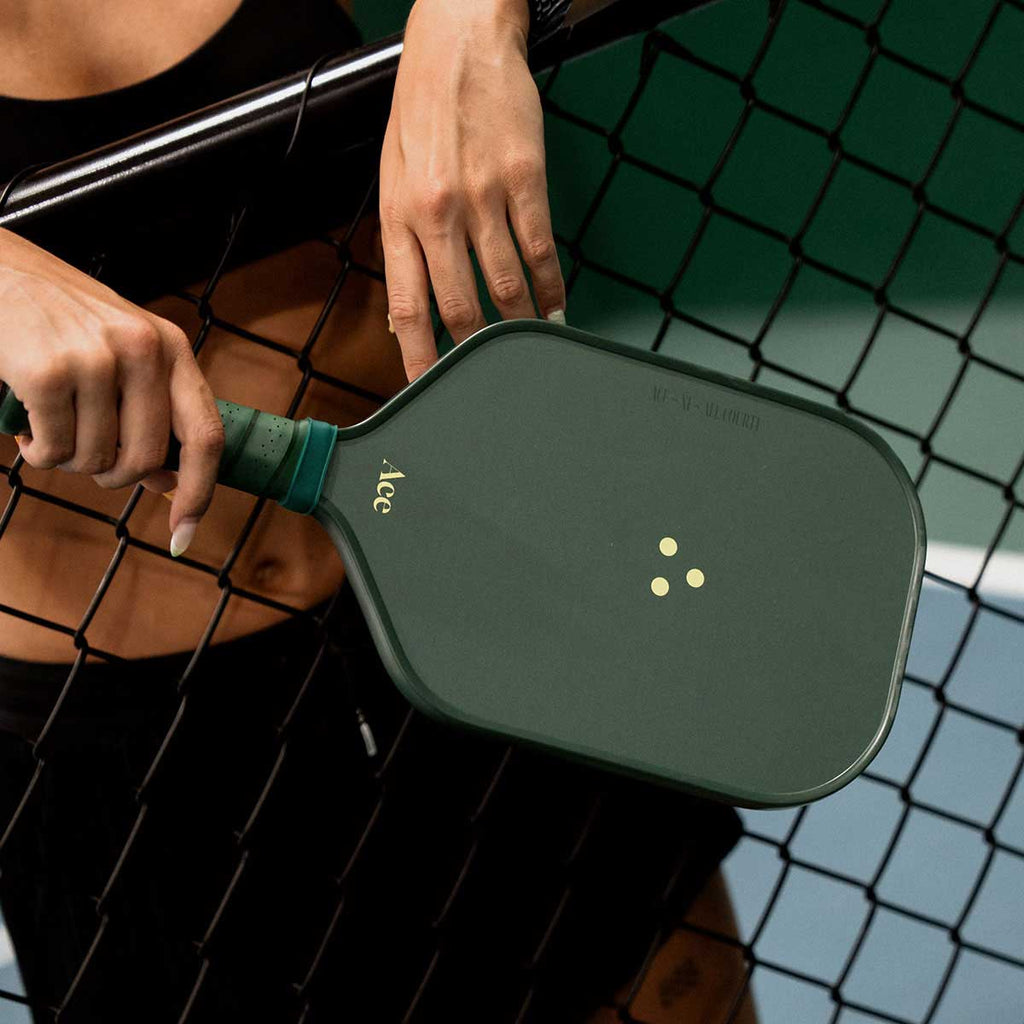 Person holding a green pickleball paddle on a court